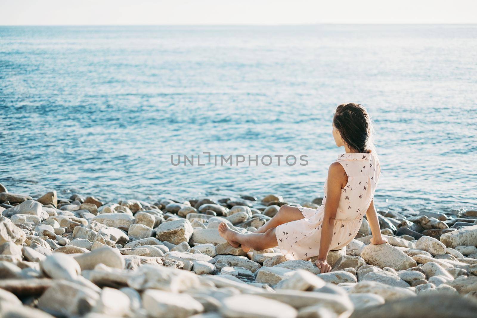 Beautiful young woman resting on pebble coast and enjoying view of sea