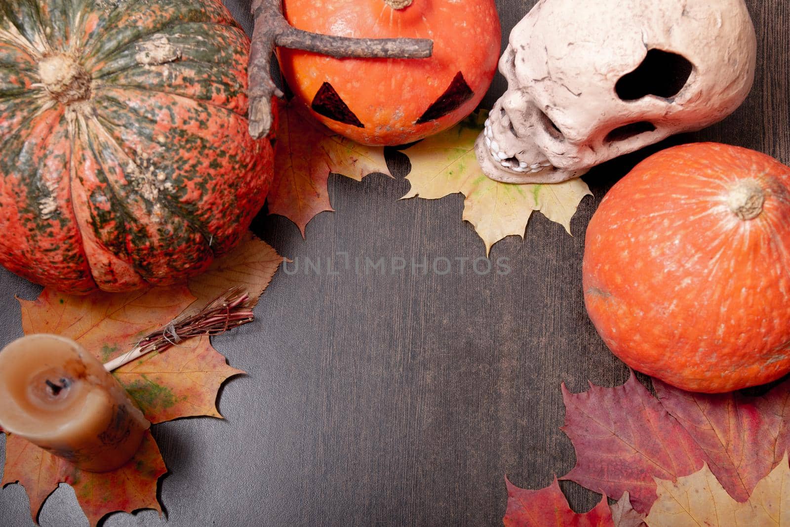 ceramic skull, candle, decorative broom and halloween pumpkins on a dark brown table background, autumn leaves and cones, copy space, top view