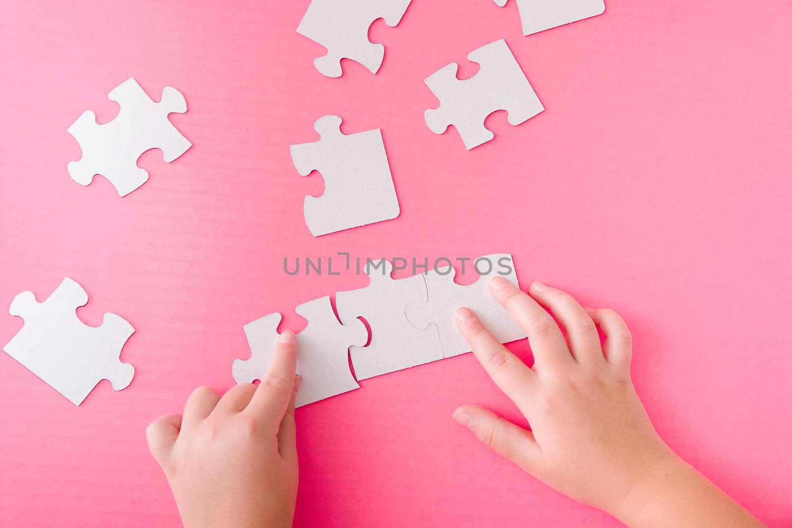 children's hands stack paper white puzzle on pink background by natashko