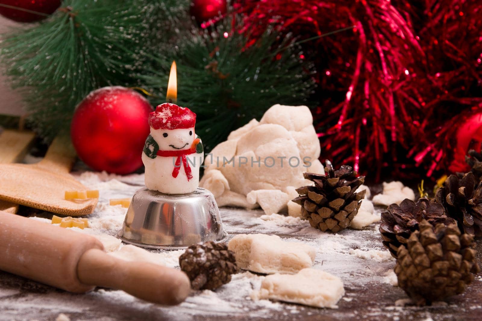 a snowman candle is burning against the background of Christmas tree decorations, making New Year's cookies, dough, cheesecake, cones in the background