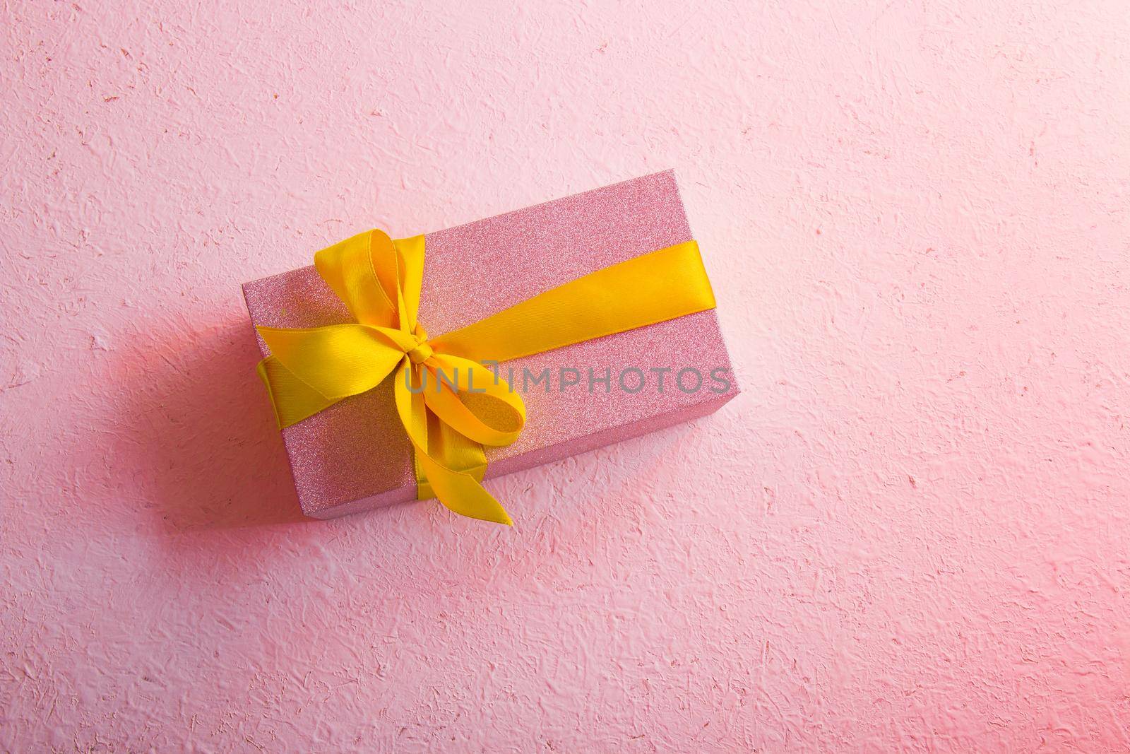 pink shiny gift box on a pink background with a gold bow top view place copy pink light