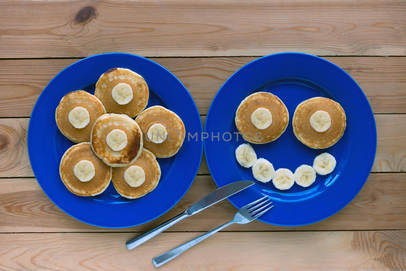 Pancakes with smile and flower image on blue plates and wooden background. banana fruit smiling breakfast - fun food for kids
