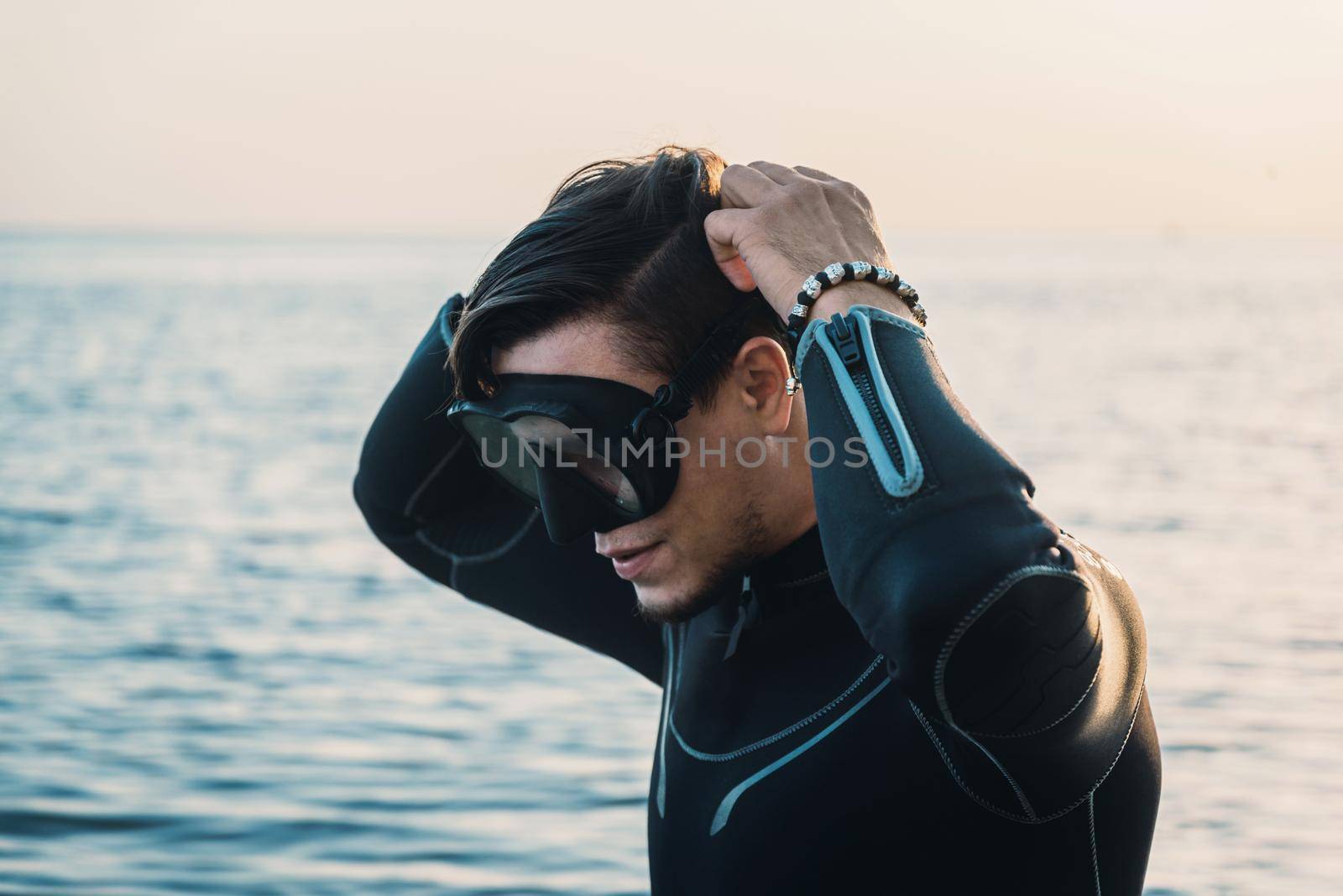 Diver young man putting on a mask on background of sea