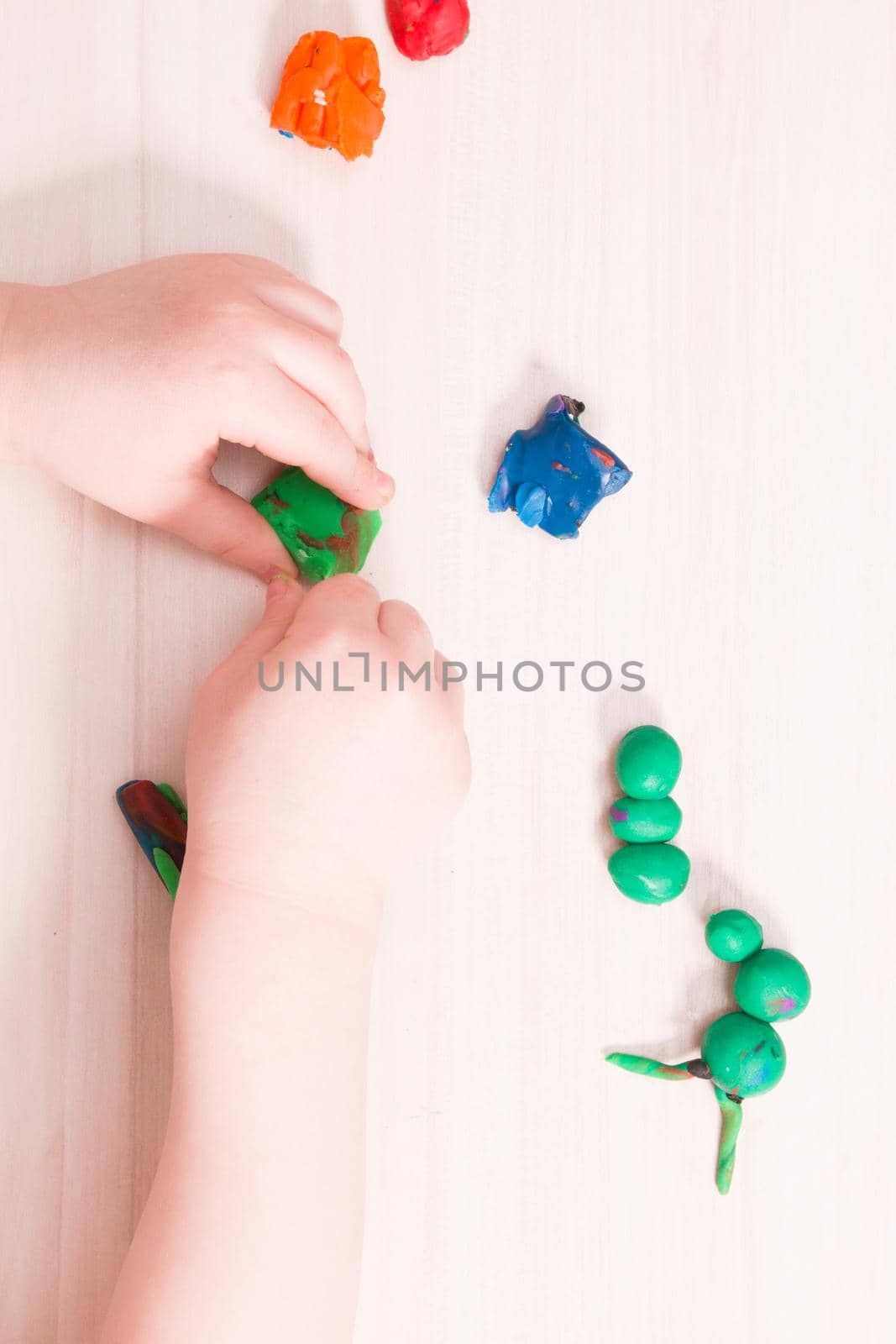 a small child sculpts a caterpillar from green plasticine on a wooden table, developing fine motor skills of hands, playing with a child at home, preparing for kindergarten, stay at home