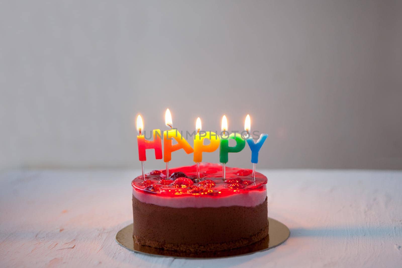 chocolate cake with rainbow candeles-birthday greetings HAPPY from burning candles on white background