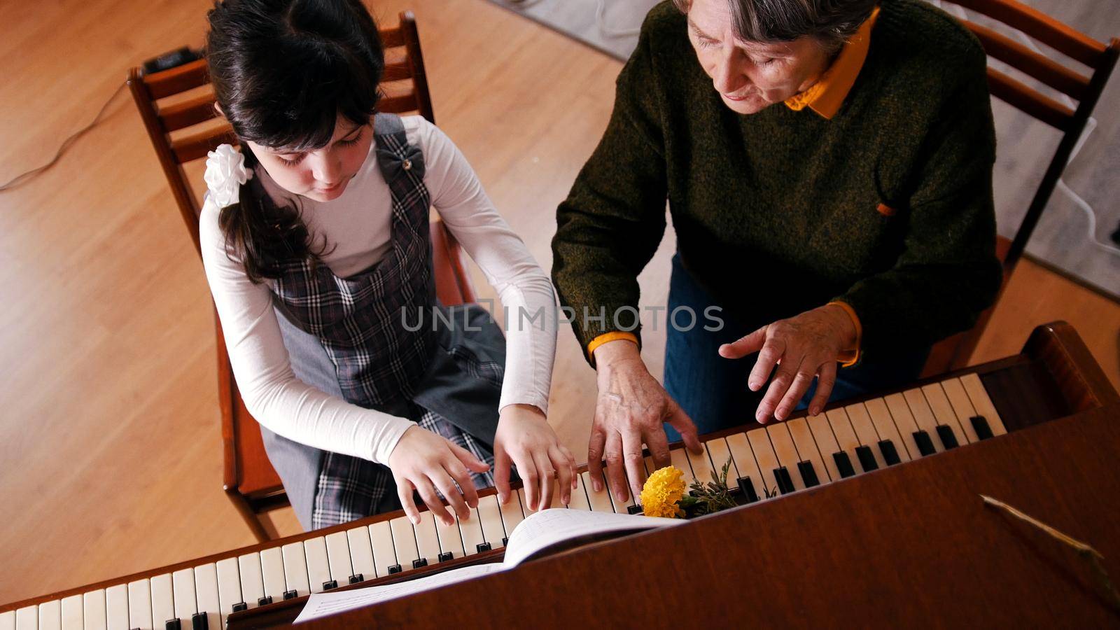 A little girl playing piano on music lesson. A teacher helping her. Upper angle by Studia72