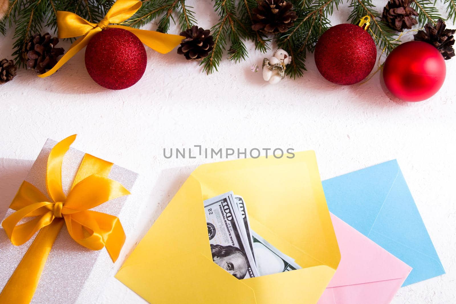 money in an envelope, gift box with a golden bow and Christmas ornaments on a white background, Christmas toys, cones, fir branches, frame