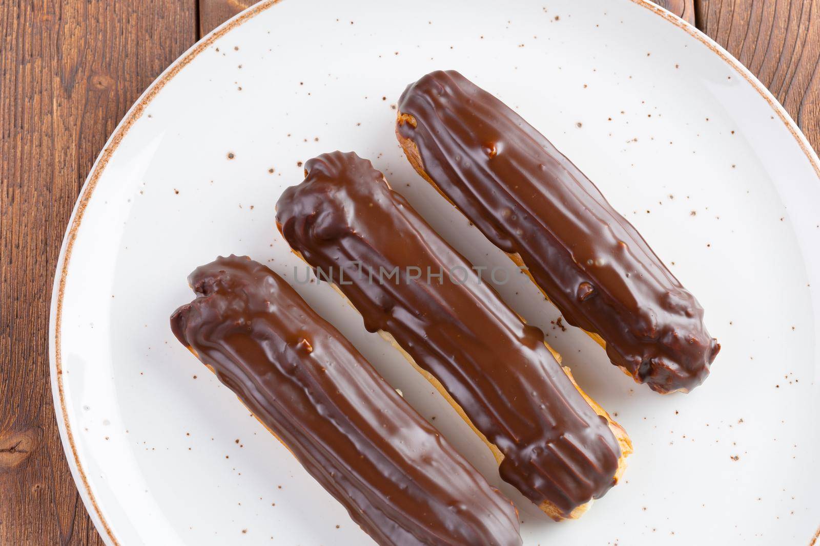 Chocolate eclairs on white plate on wooden table close up