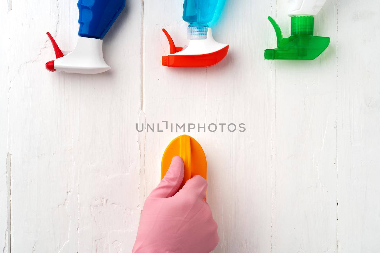 Hand in glove with cleaning supplies above white wooden background, top view