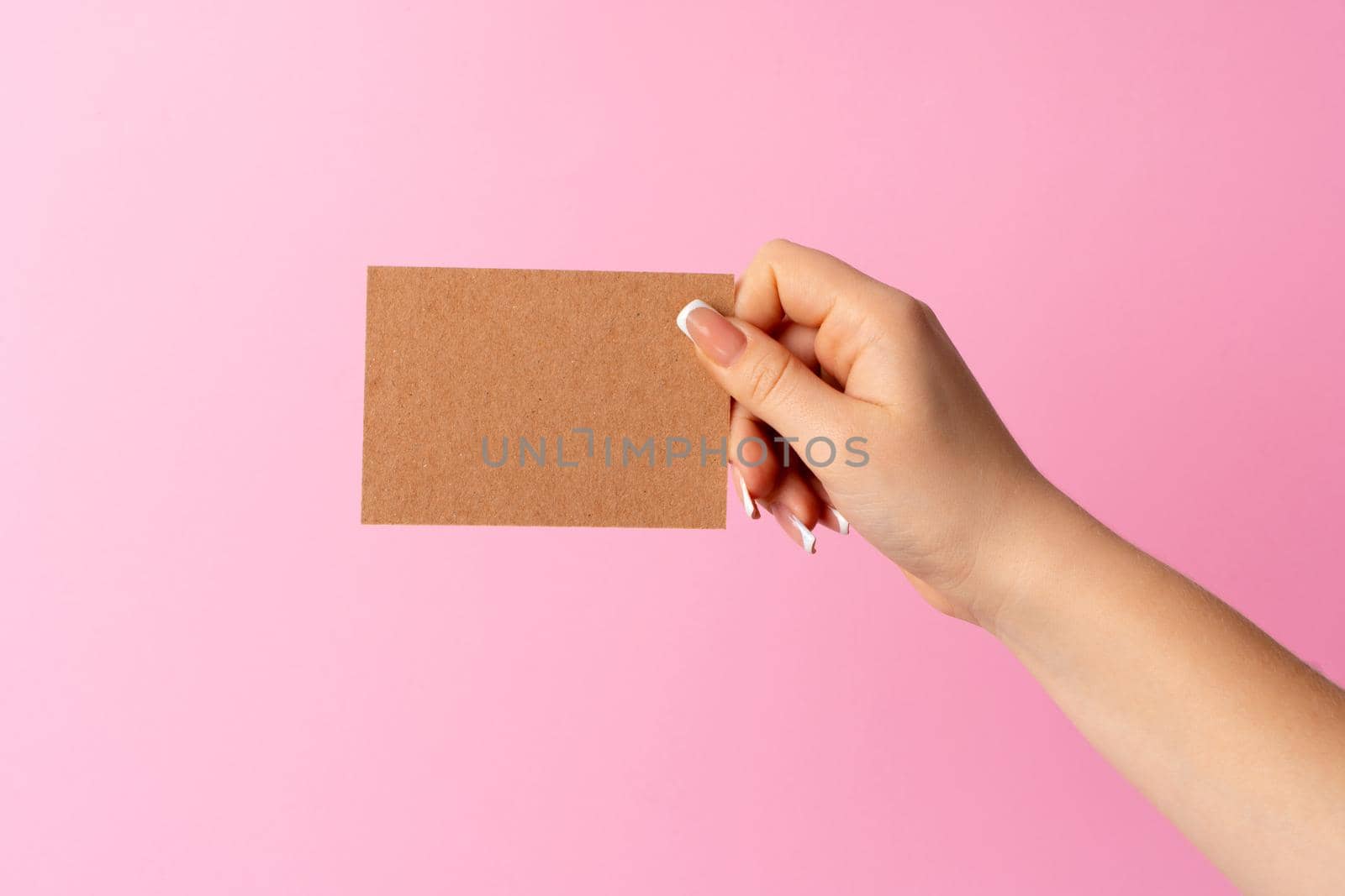 Woman hand showing blank business card on pink background. Close up.