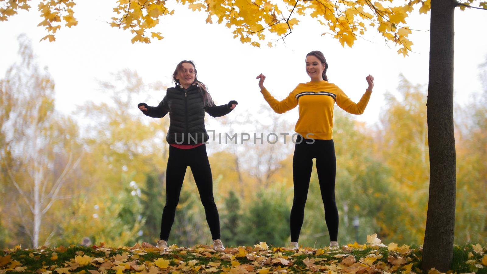 Acrobatic girls in jackets warming up outside before training in park. Hands to the sides. Autumn by Studia72