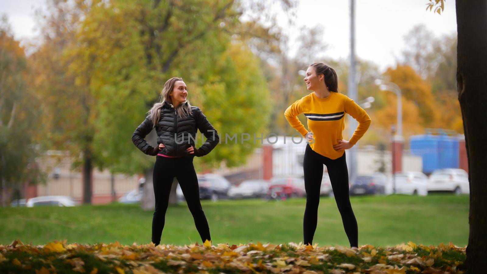 Girls warming up outside before training in park. Hands to the sides. Autumn. by Studia72