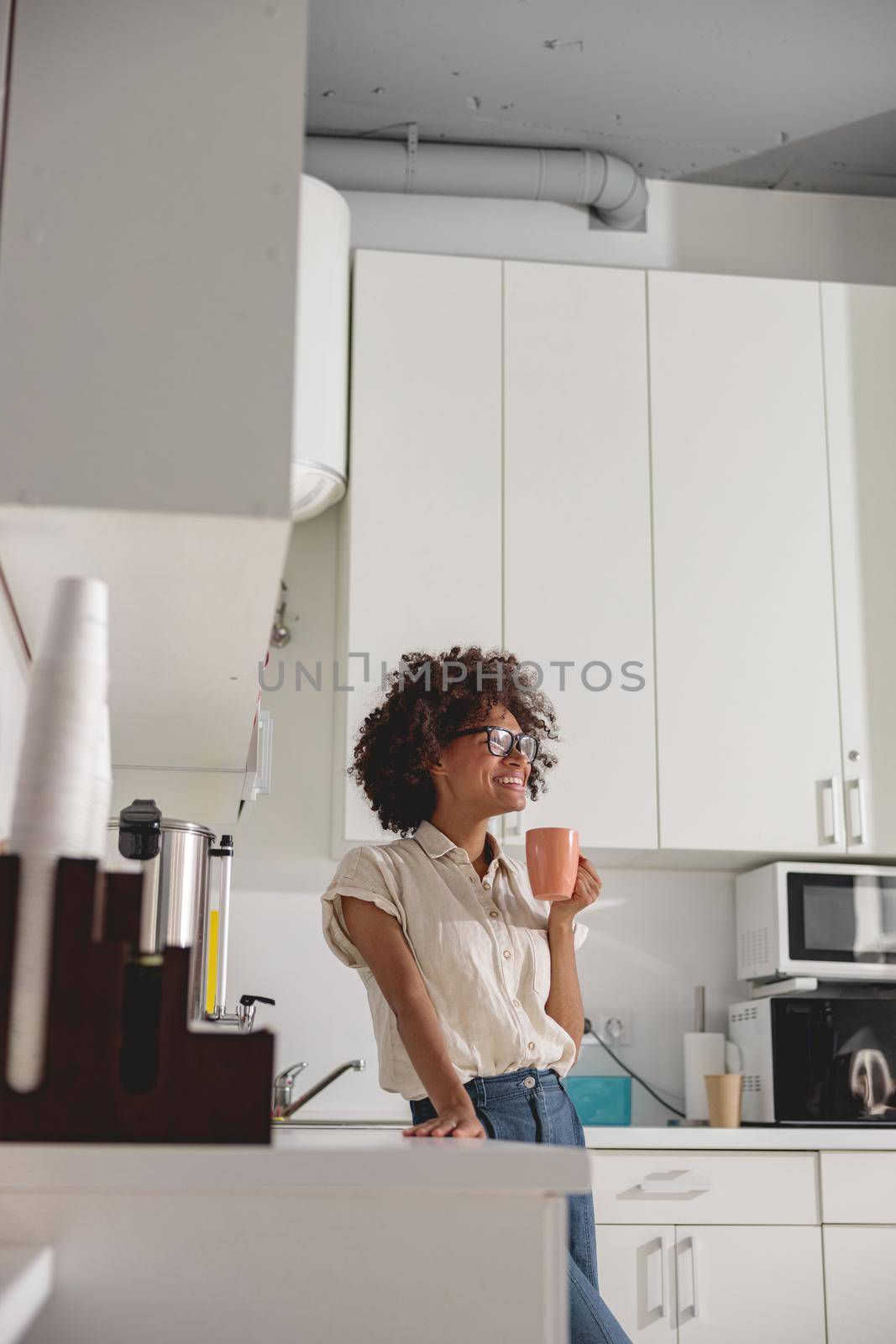 Happy Afro American worker wearing glasses and standing in modern office kitchen interior