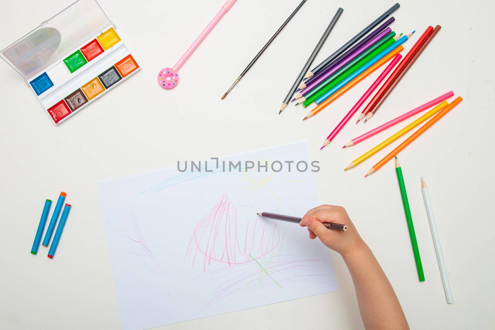 child draws with crayons on white lsita on a white table top view copy space