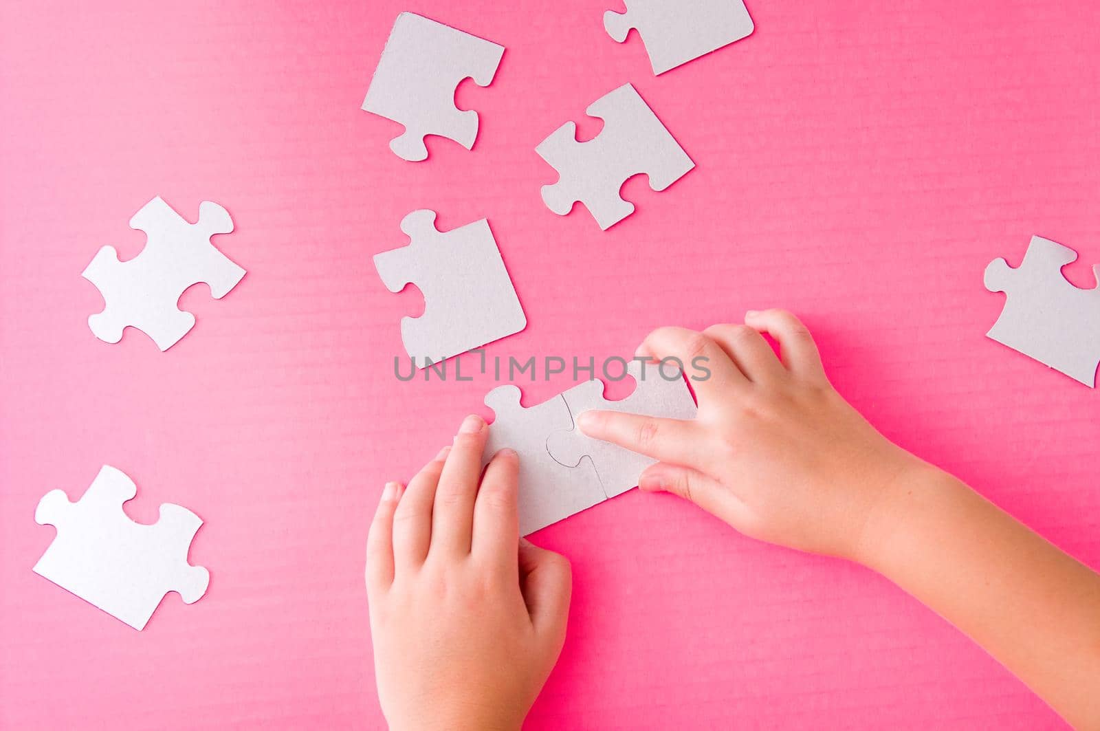 children's hands stack paper white puzzle on pink background by natashko