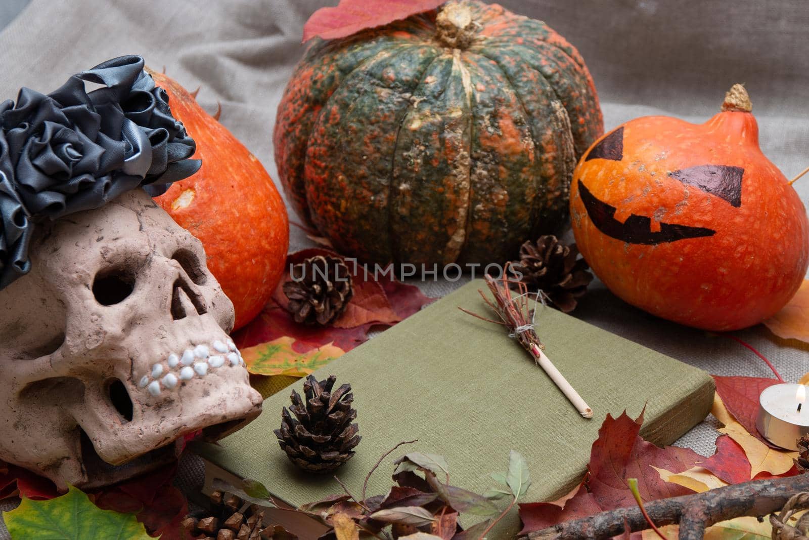 ceramic skull in a wreath of flowers from black ribbons, cones, autumn leaves, a candle and pumpkins, a jack head, a witch book, blurred background, halloween background