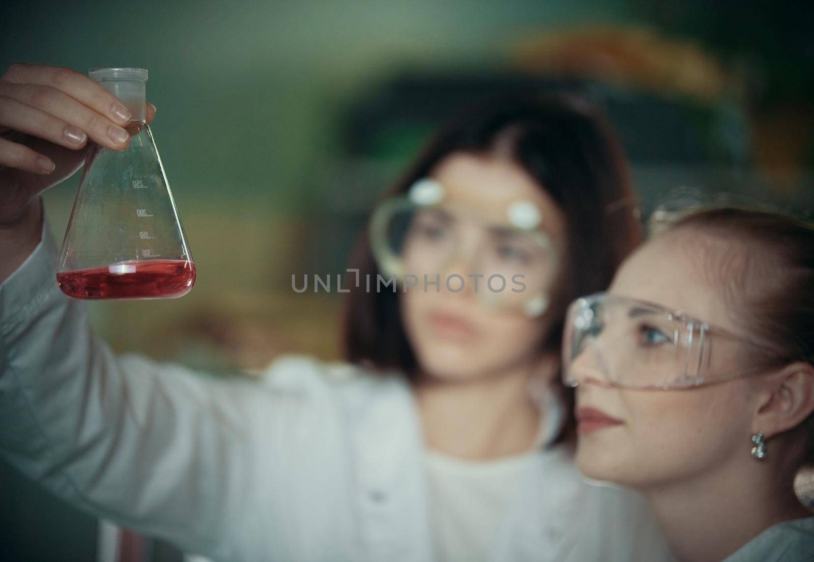 Chemical laboratory. Two young woman holding a flask with red liquid in it. Close up