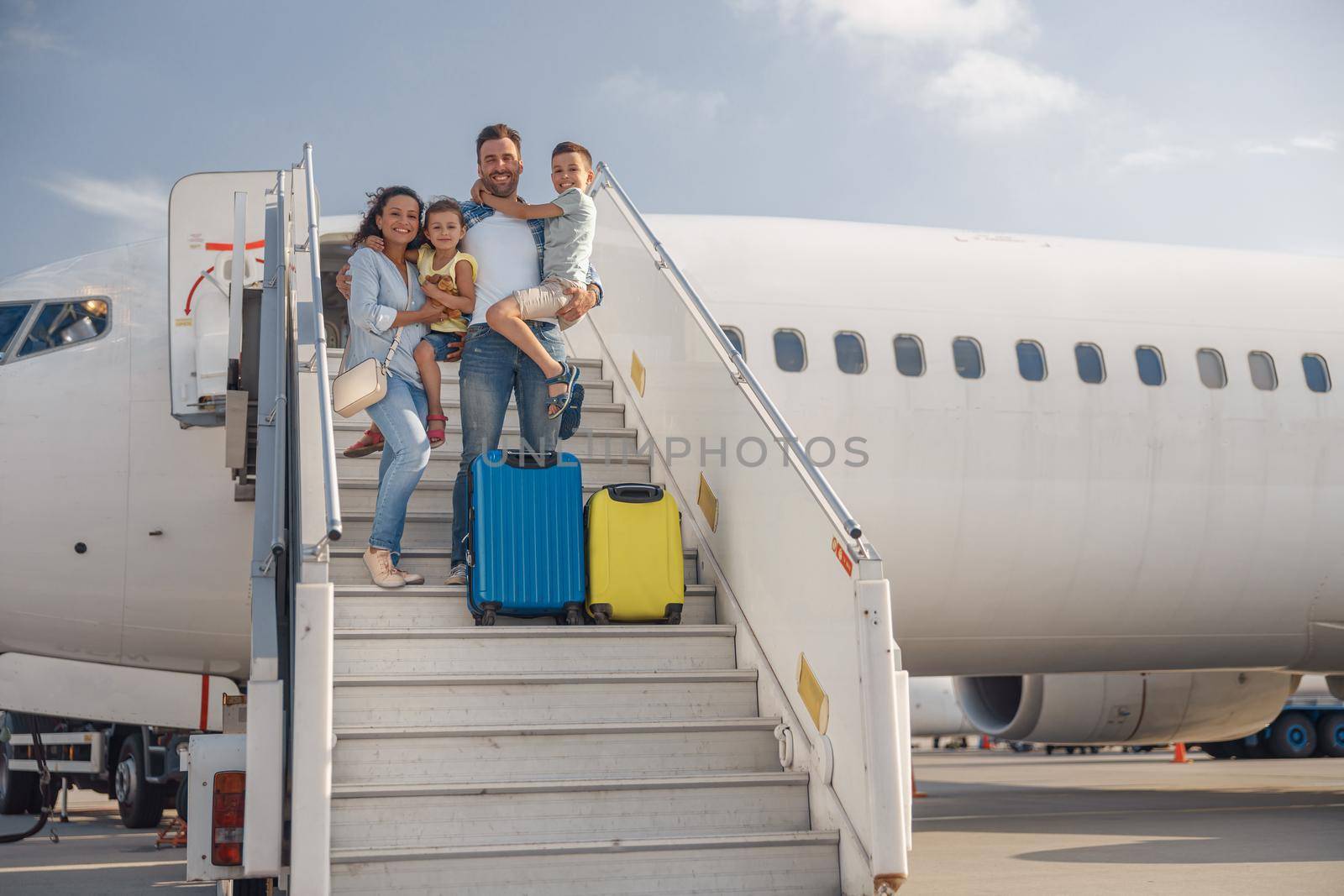 Happy family of four standing on airstairs, getting off the plane on a daytime. People, traveling, vacation concept