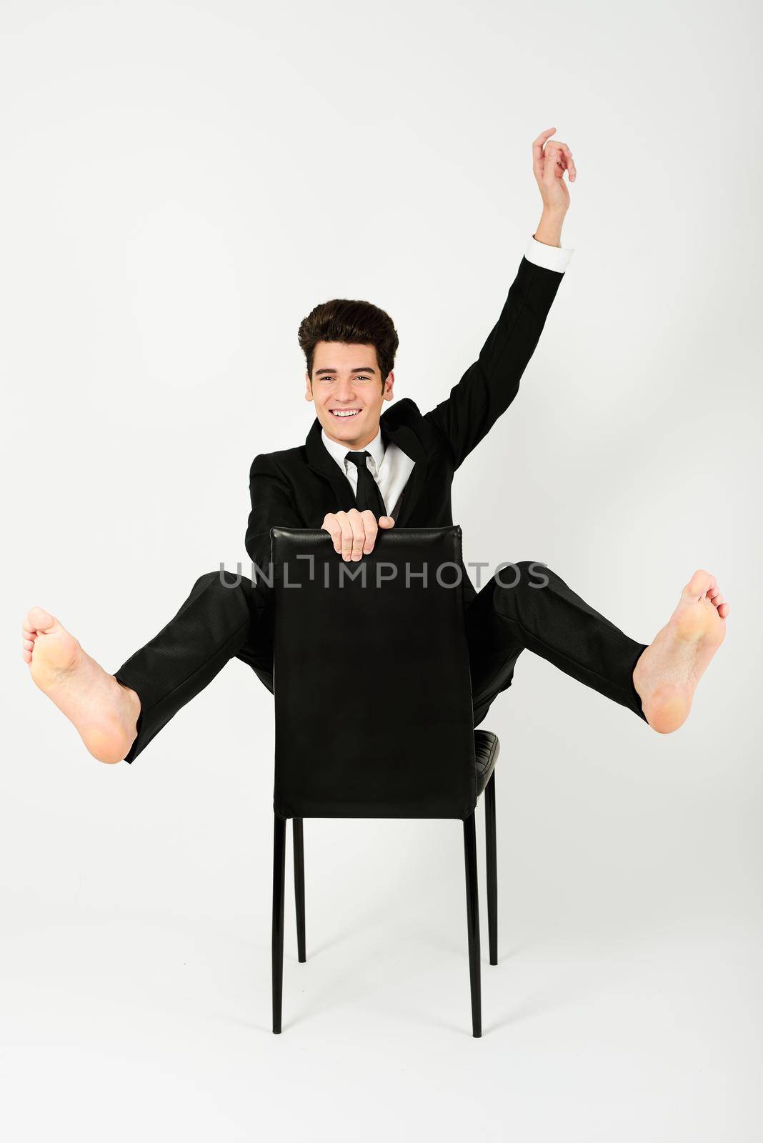 Portrait of a happy young businessman sitting in a chair with raised arm, on white background