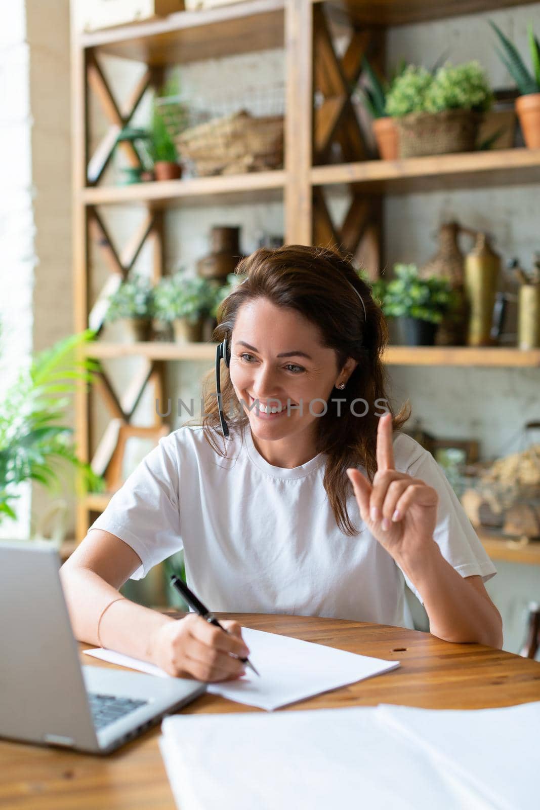 Smiling woman working at home in front of a laptop monitor. She held up her finger to indicate the importance of the idea. Modern technology concept.