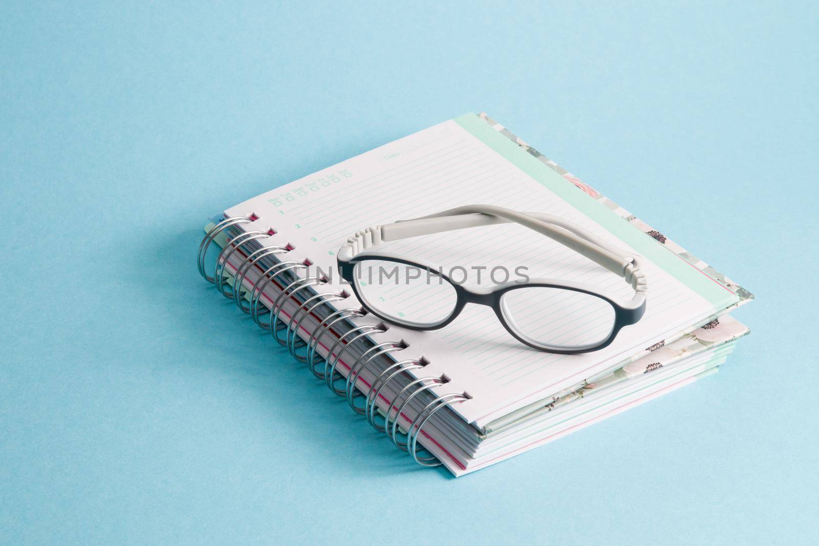 children's glasses lie on a notebook, blue background, copy space, gray bending anti-vandal glasses frame