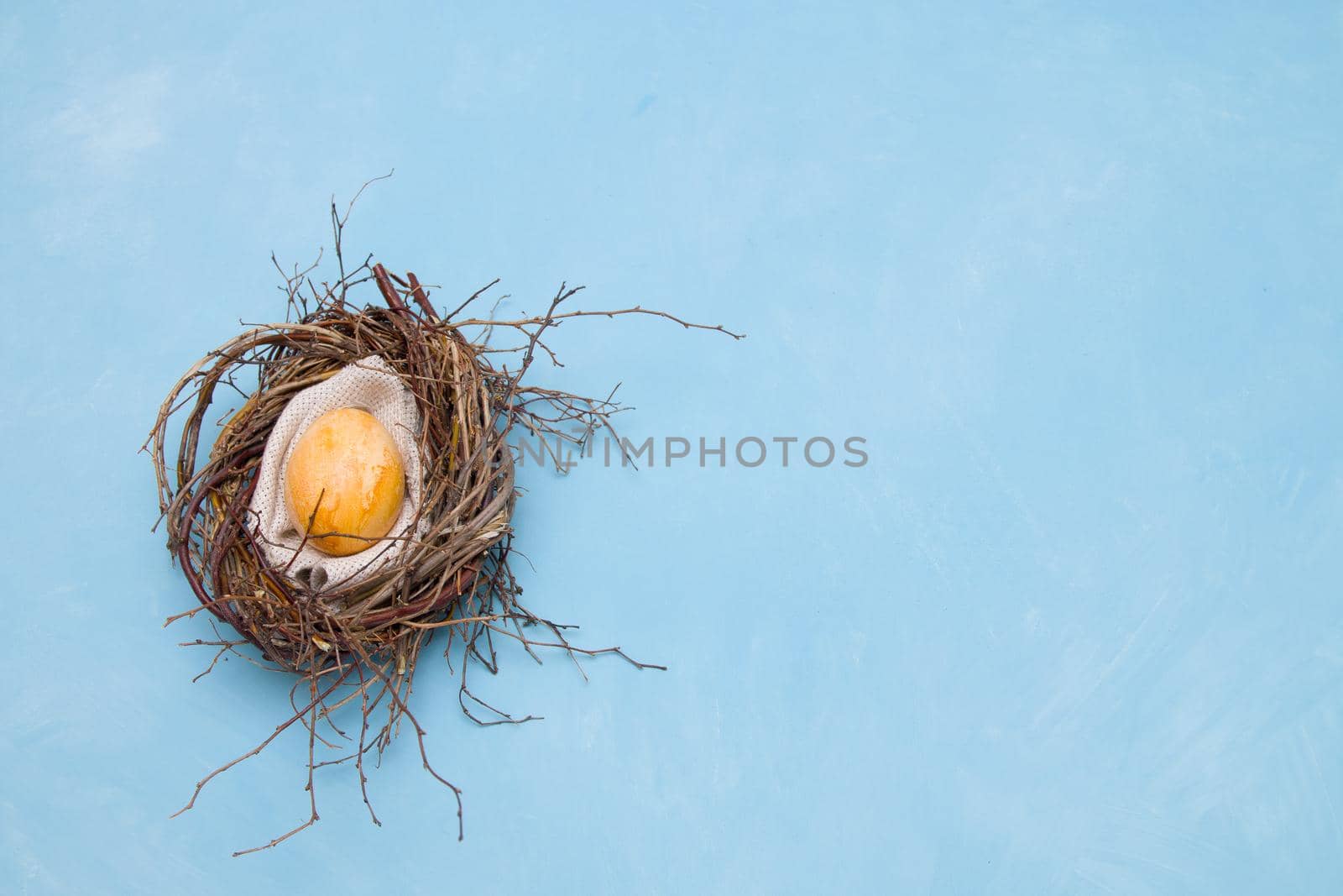 golden easter egg in a makeshift nest on a blue background copy space top view