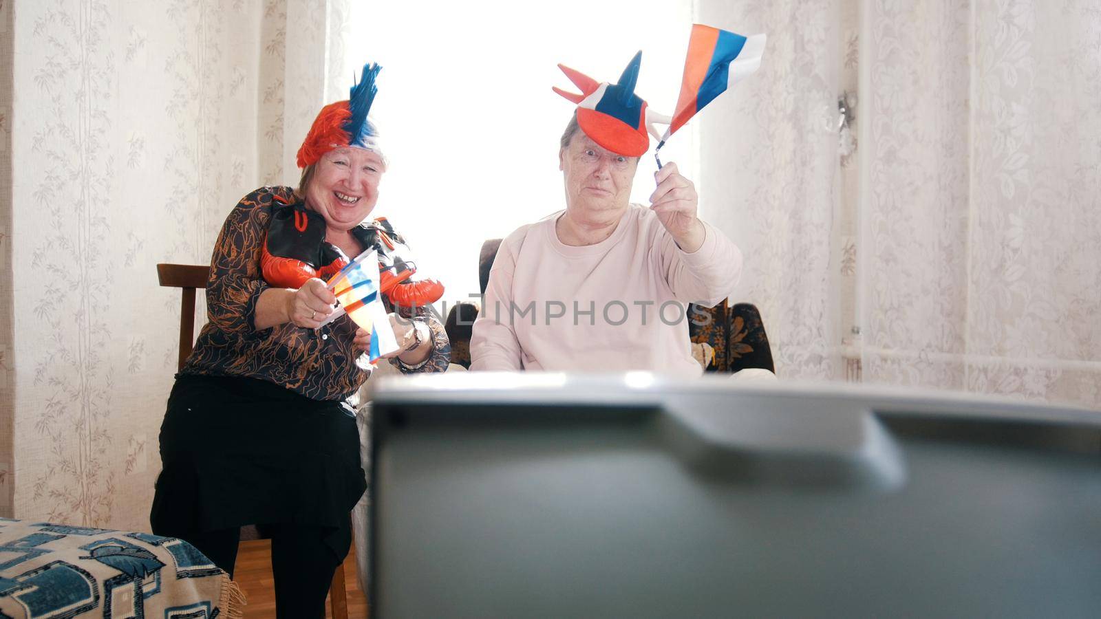 Two elderly women watching in russian accessories TV. Having fun. Portrait