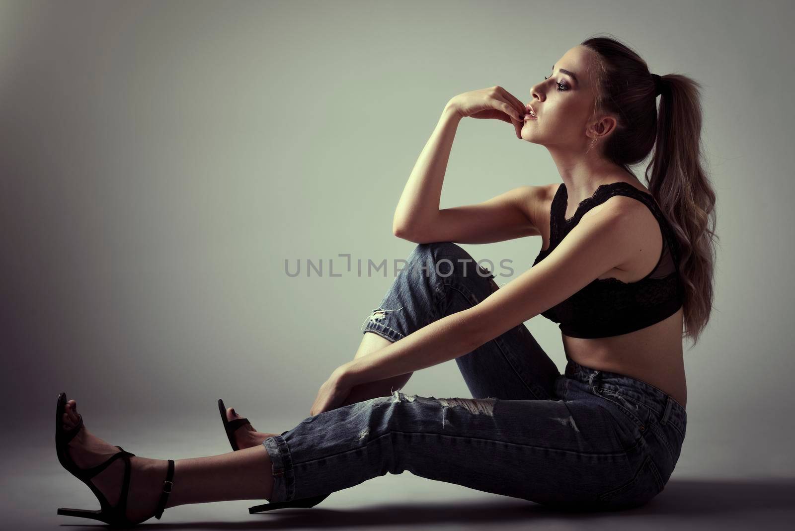 Young woman wearing black bra and blue jeans sitting on floor. Studio shot. by javiindy