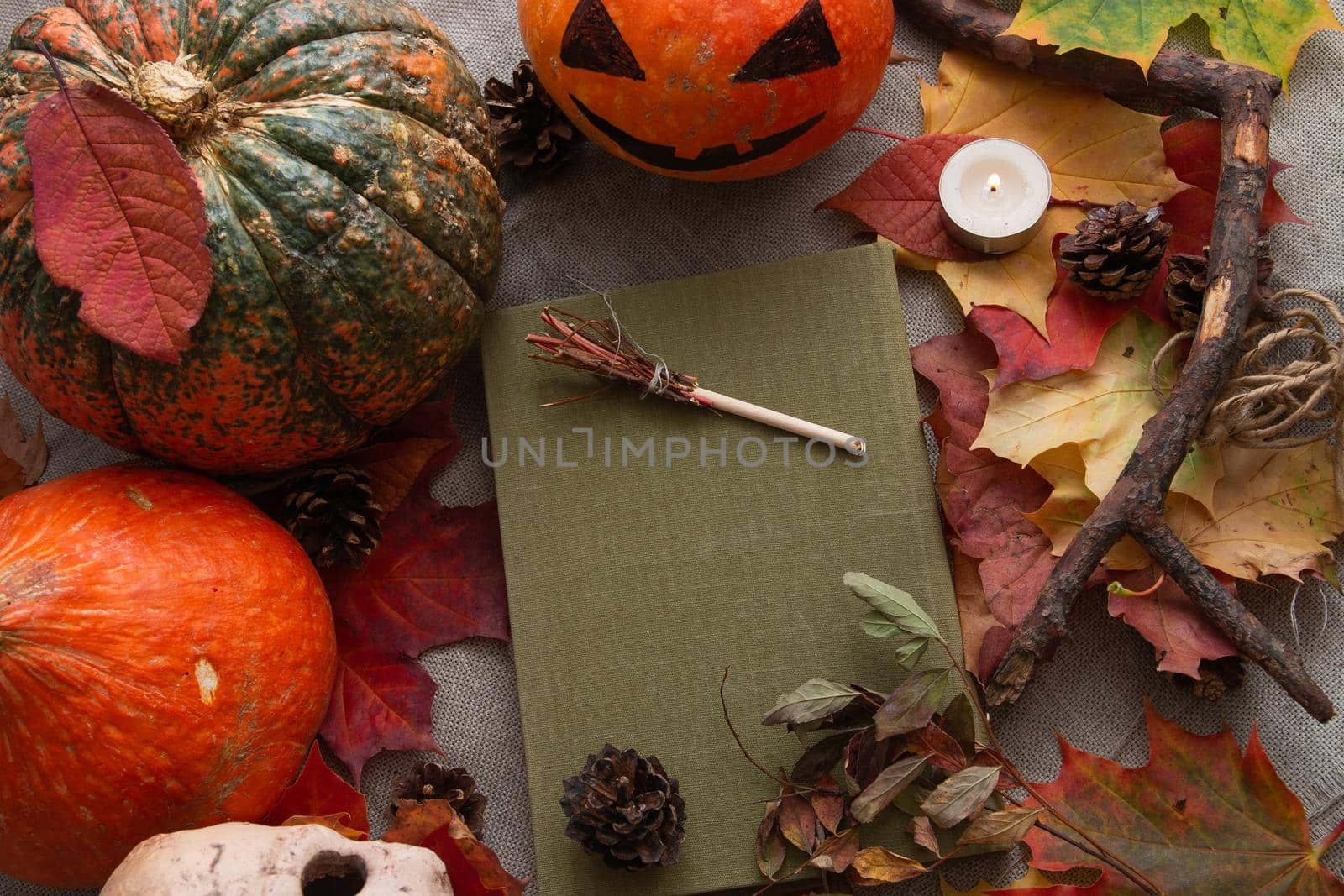 scoop, book and pumpkins on autumn leaves, a candle burns, decorative broom of a witch and cones, halloween composition, background, holiday preparation