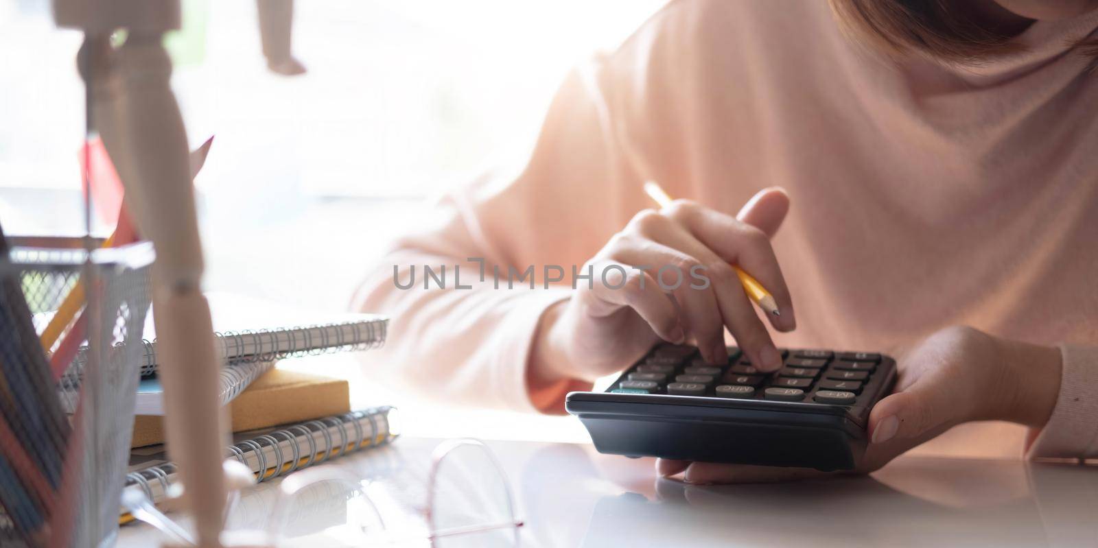 woman hand working with calculator and holding yellow pencil with nature green leaves background..