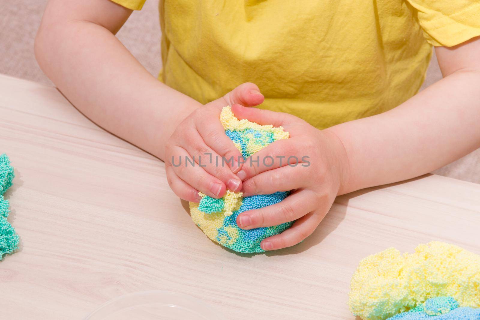 the child plays plasticine from polymer granules at the table, the original plasticine from tiny balls, the development of fine motor skills of hands, playing with the child at home