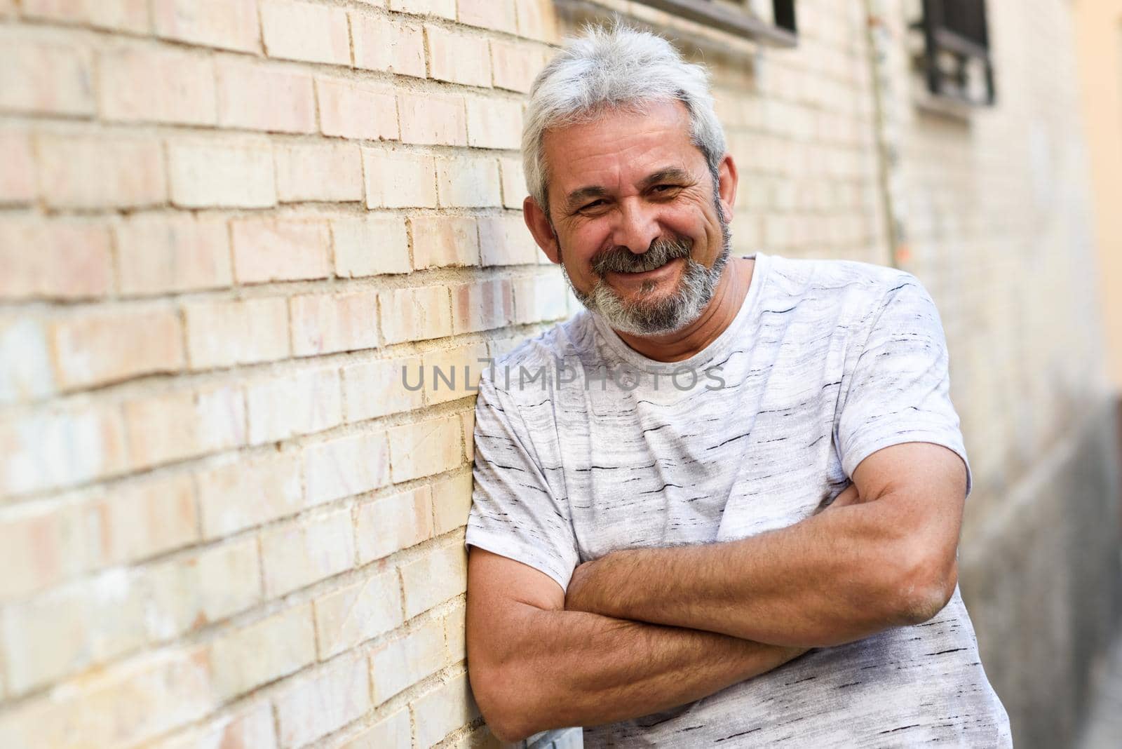 Mature man smiling at camera in urban background. Senior male with white hair and beard wearing casual clothes.