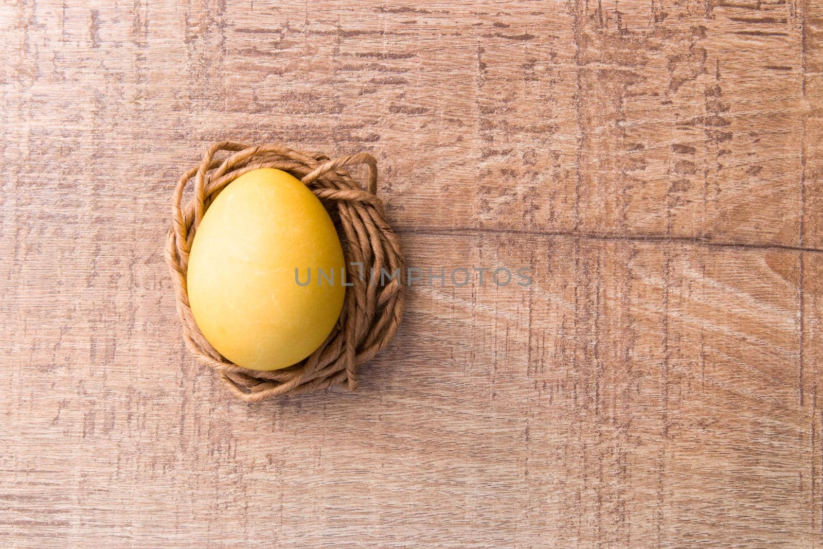 yellow egg on a nest of paper thread, wooden background, copy space, easter background