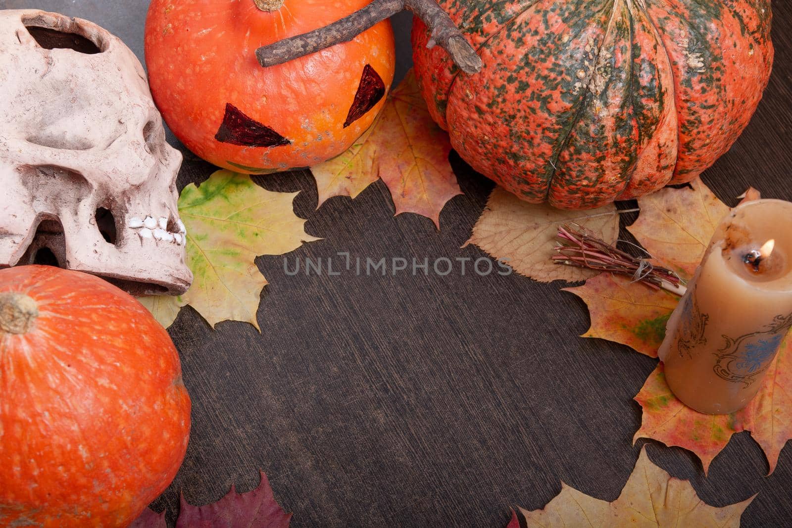ceramic skull, candle, halloween pumpkins on a dark brown table background, autumn leaves and cones, copy space, top view