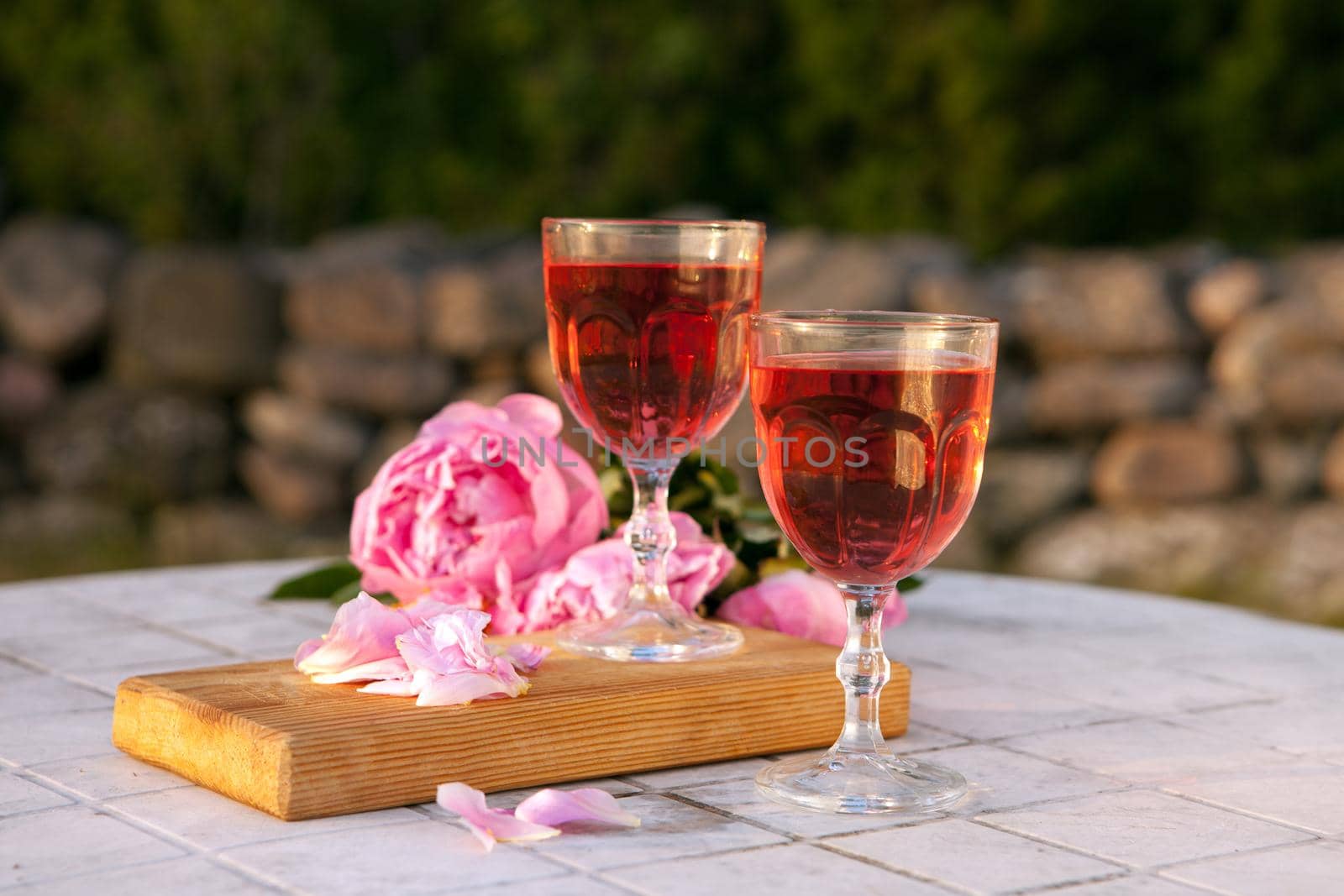 two glasses with rose wine and pink peony bouquet. delicious refreshing drink, huge blossoming flowers at the table at sunset