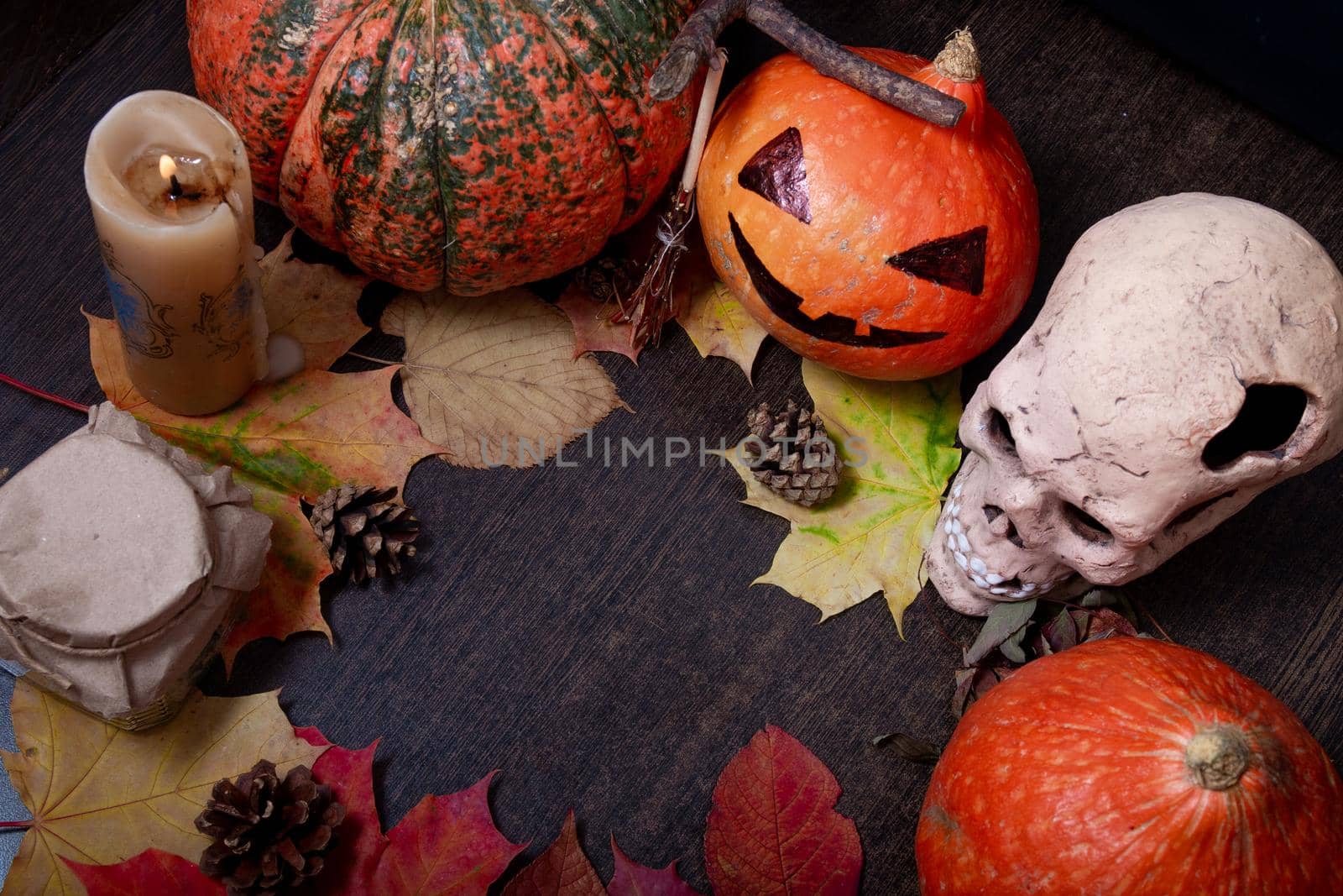 ceramic skull, candle, decorative broom and halloween pumpkins on a dark brown table background, autumn leaves and cones, copy space, top view by natashko