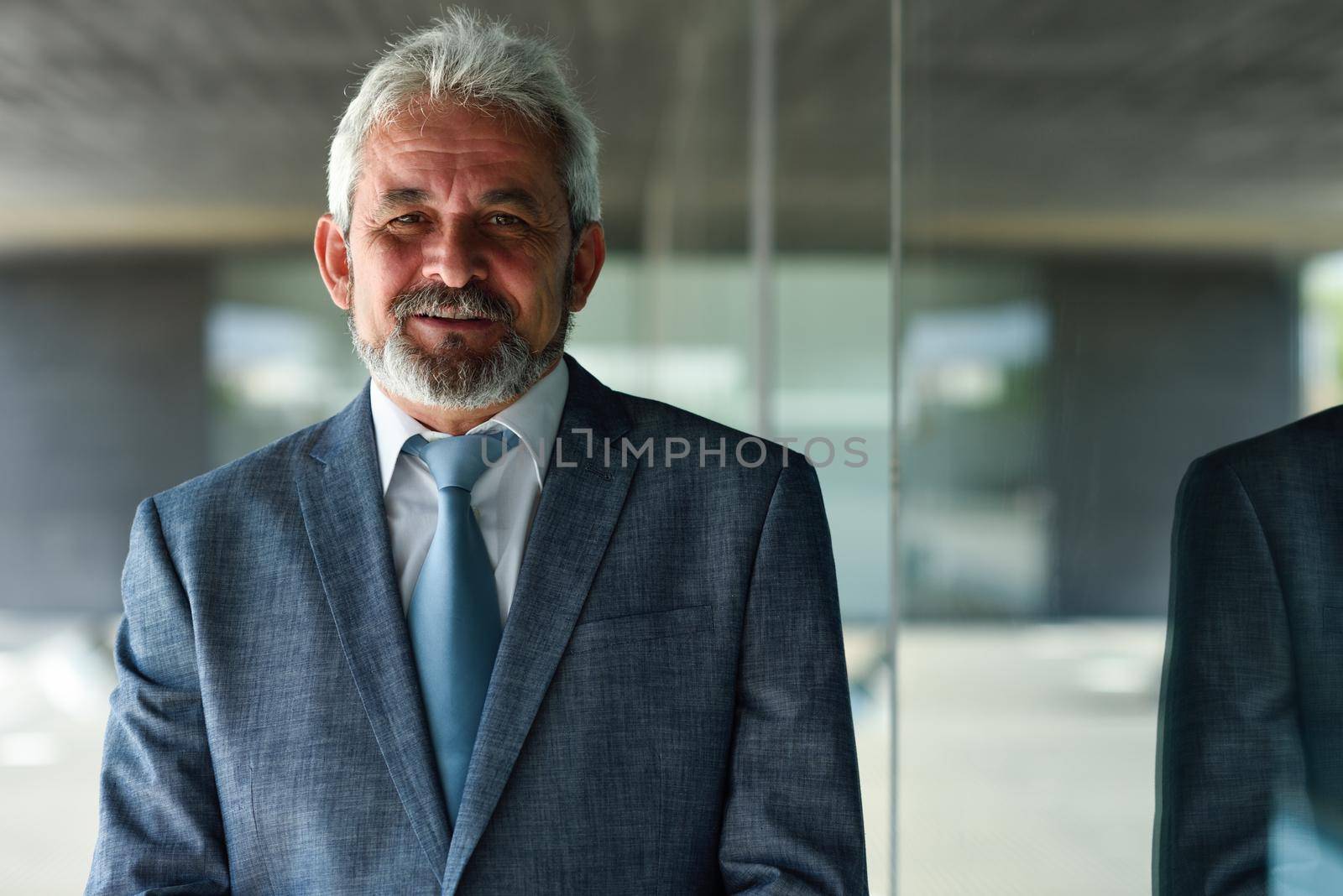 Senior businessman looking at camera outside of modern office building. Successful business man in formal smiling in urban background.