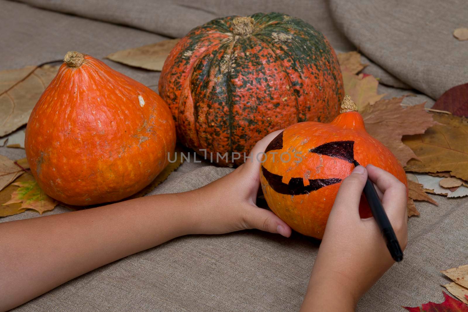 the child draws a pumpkin face on a black market, jack o lantern, halloween background, preparation for the holiday