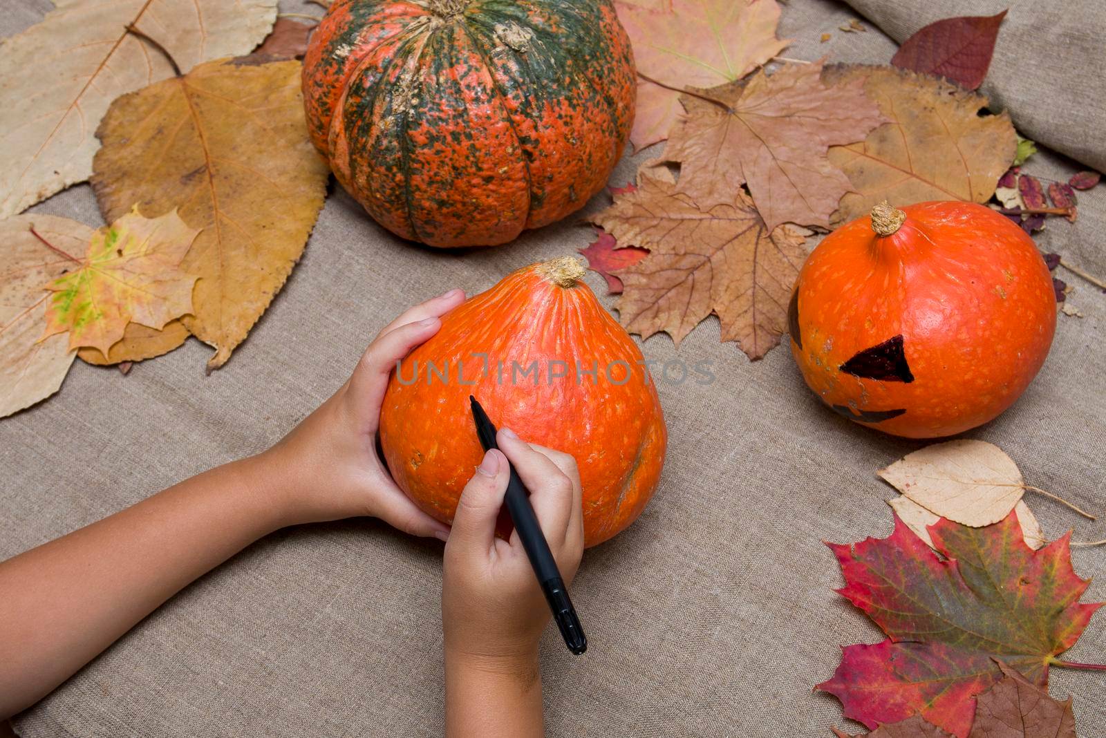 the child draws a pumpkin on the face with a black market, jack-o-lantern, halloween background, preparation for the holiday, pumpkins, fabric background, place of okpia, hot sale