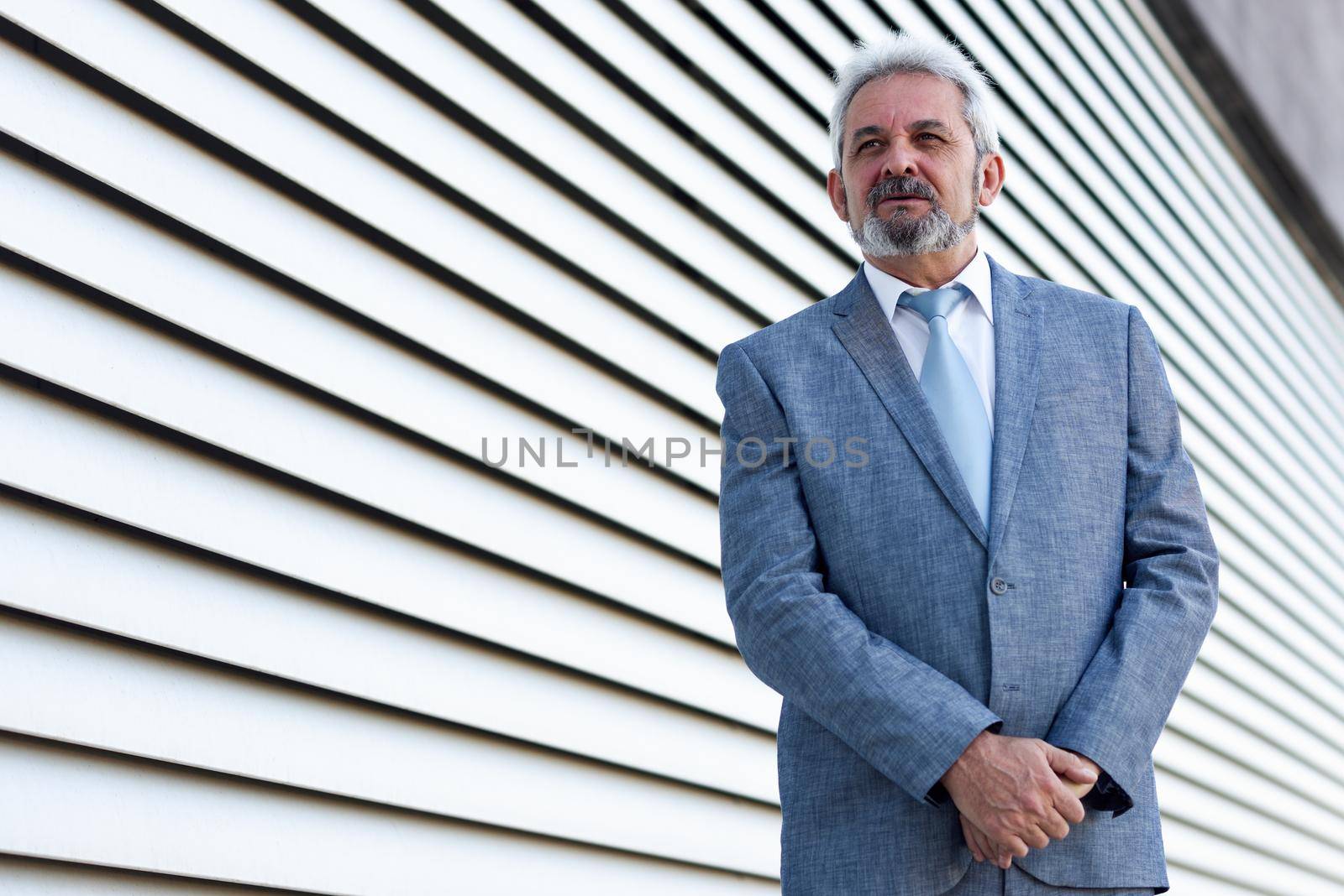 Portrait of a senior businessman with arms crossed outside of modern office building. Successful business man in formal smiling in urban background.