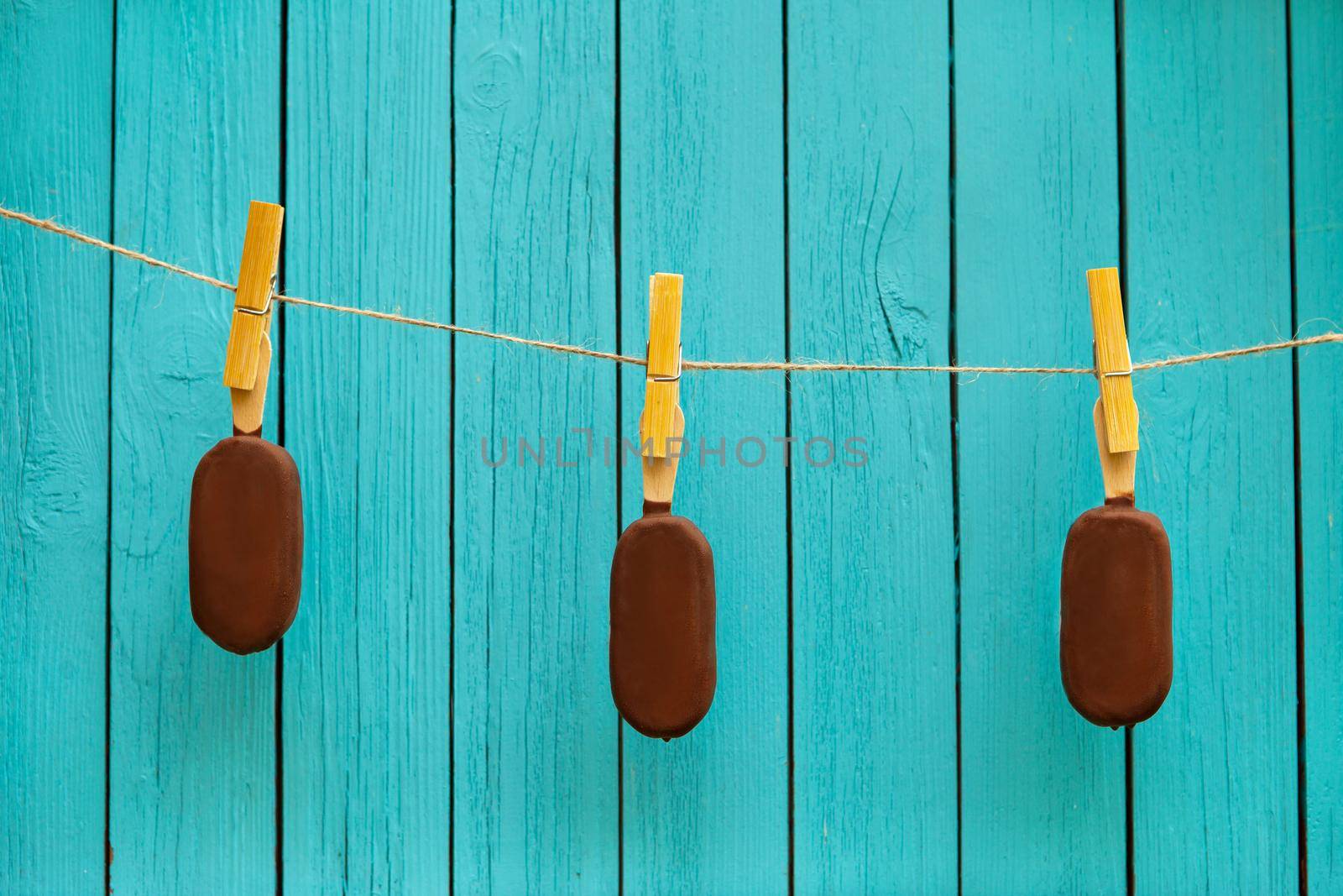 three tasty chocolate ice cream on rope near turquoise background. summer food concept