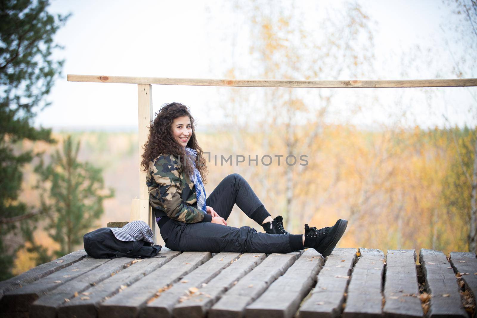 Young woman sitting on a platform on a background of the forest, smiling. Autumn