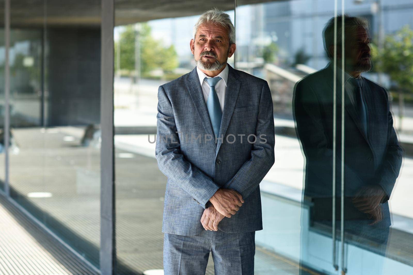 Senior businessman with arms crossed outside of modern office building. by javiindy