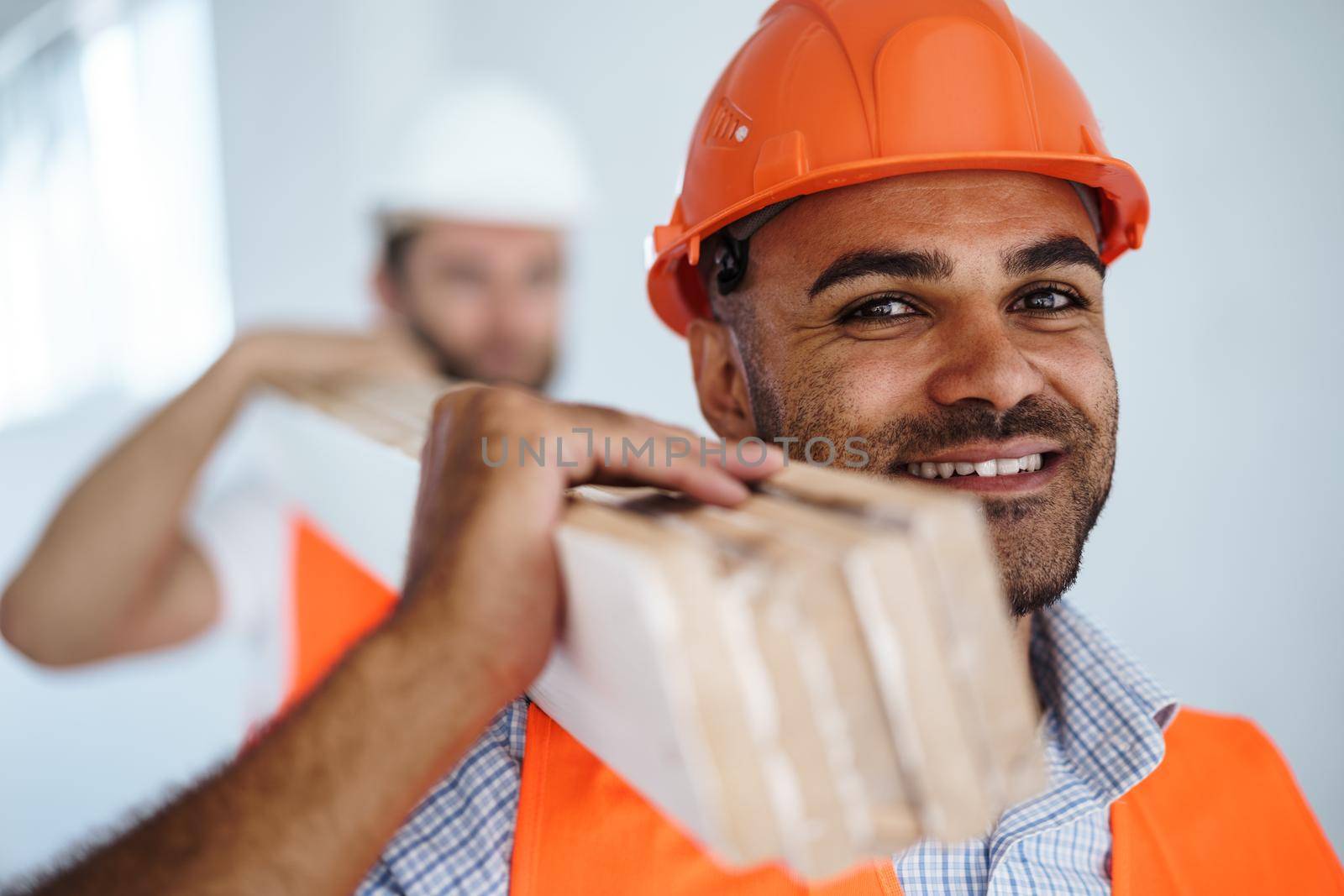 Two young men builders carrying wood planks on construction site, close up photo