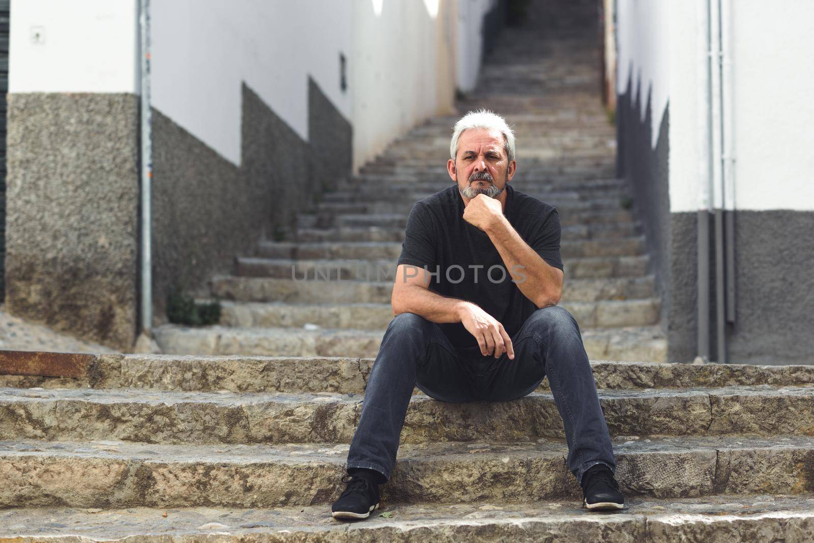 Mature man with white hair sitting on urban steps by javiindy