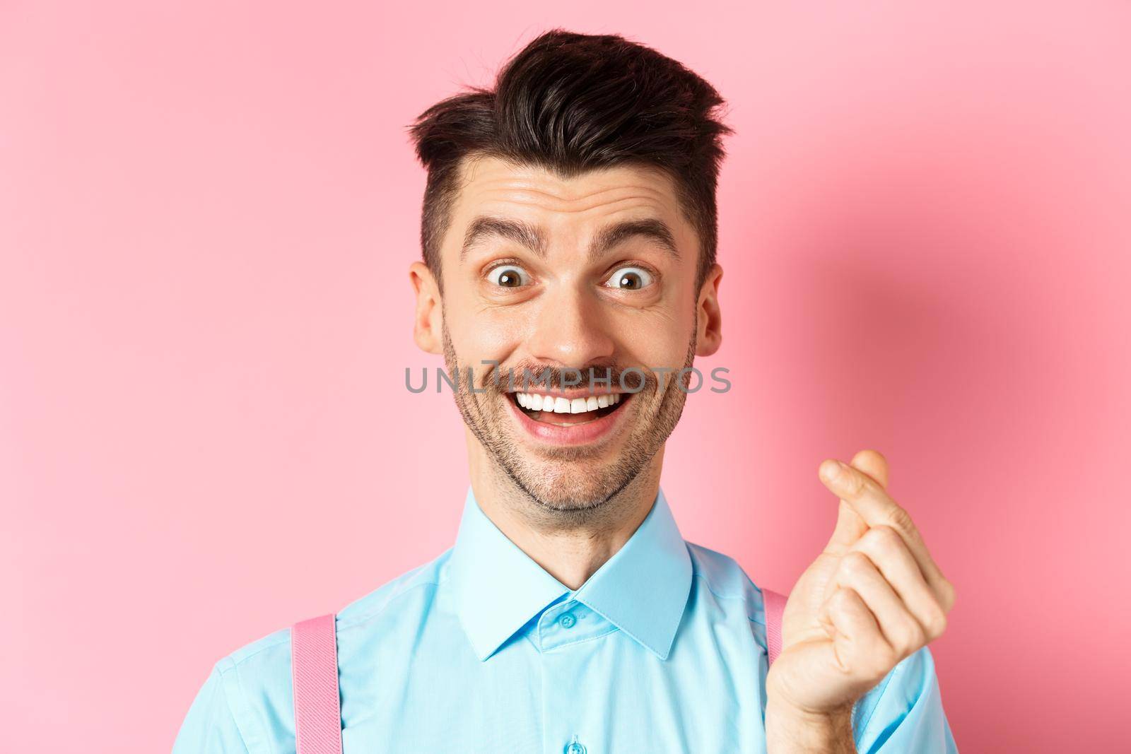 Valentines day concept. Smiling man showing finger heart and looking happy, standing over pink background by Benzoix