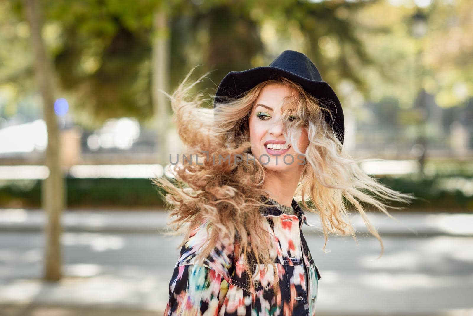 Young woman with flying hair wearing jacket and hat, happy in urban background