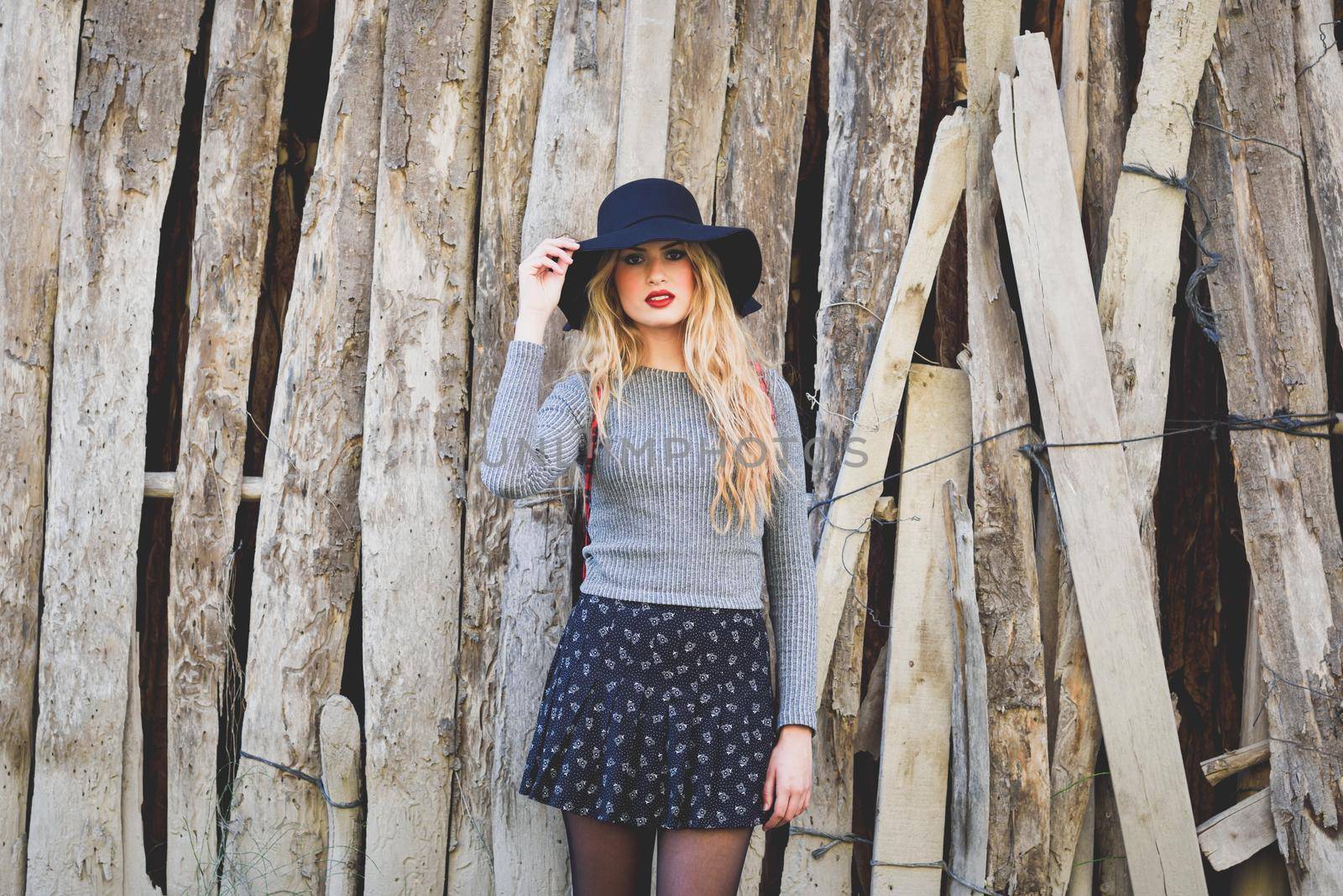 Beautiful young blonde woman, model of fashion, in rural background. Girl wearing sweater, skirt and hat.