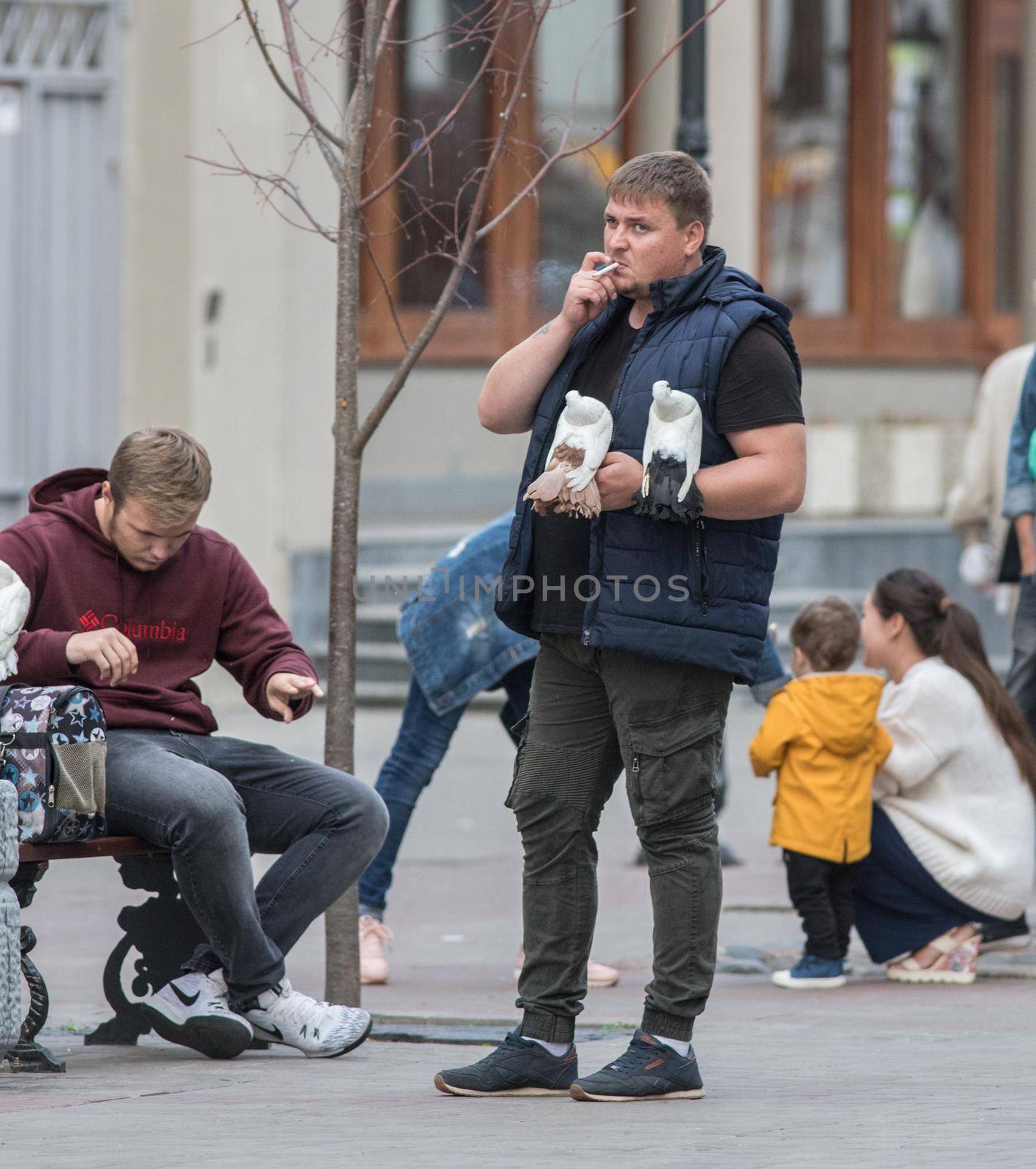 Man with hand pigeons is standing on the street and smoking. Wide shot