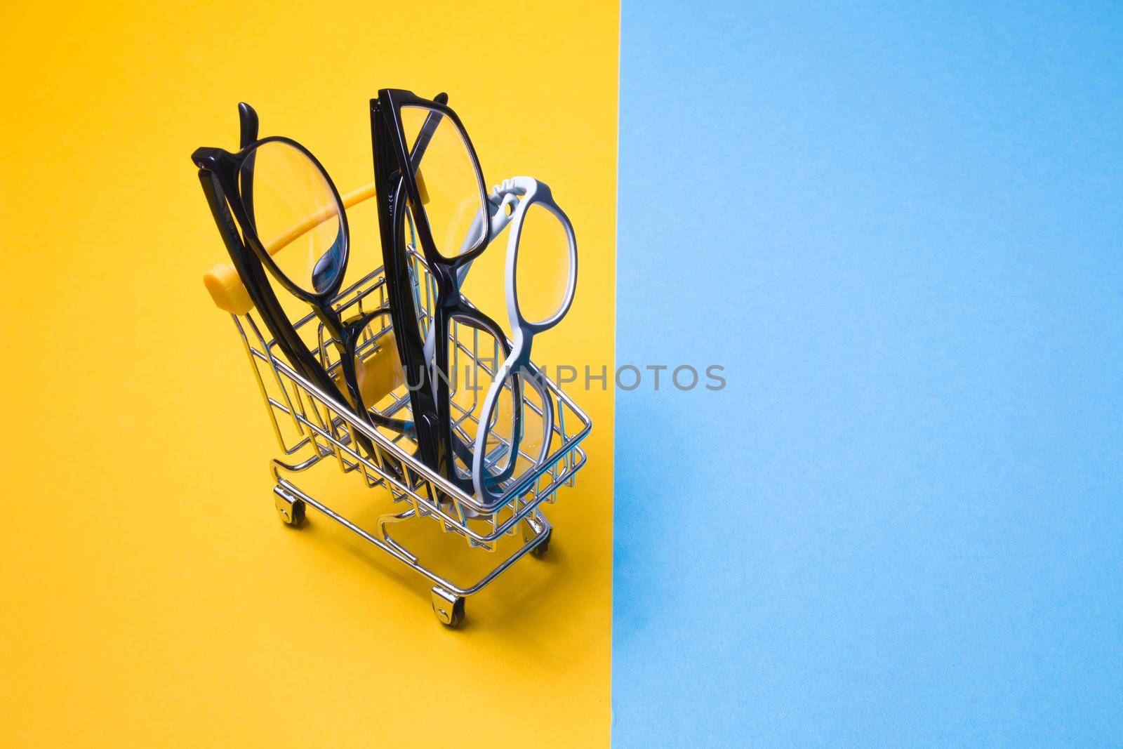 several different glasses in a small shopping trolley on a colorful background, top view, buying glasses, a store of glasses and frames for glasses, children's glasses and glasses for adults